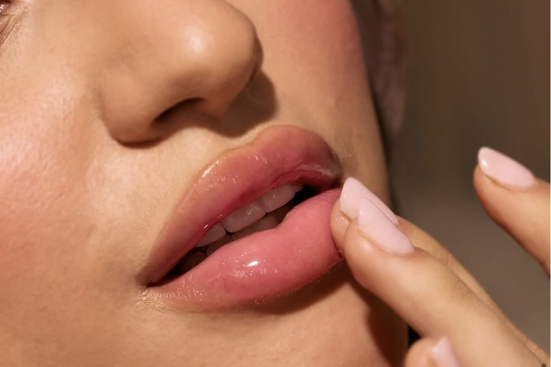 Close-up of a person's lips with a finger touching them, against a neutral background